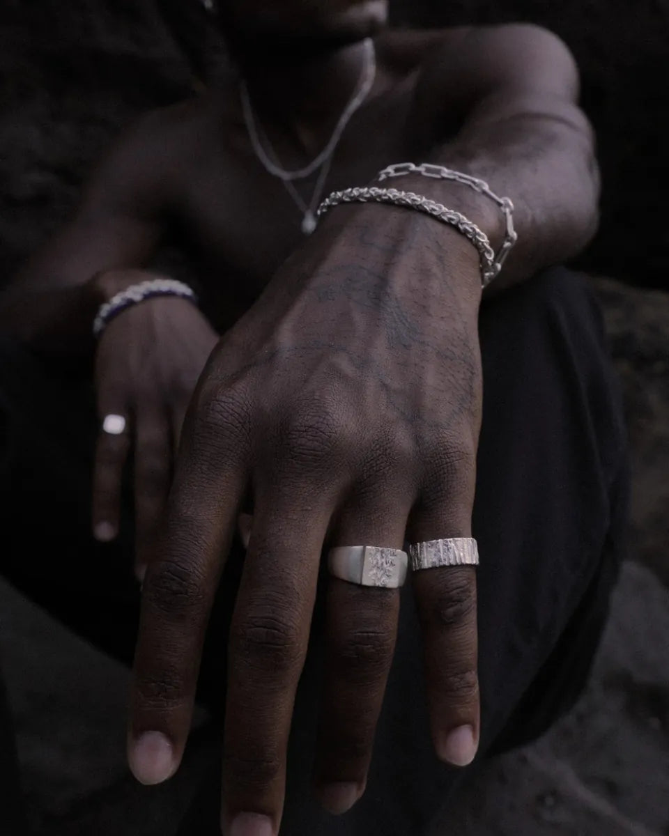 Hand mit strukturierten Silberringen und Armbändern vor dunklem Fels
